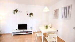 Ein modernes Wohnzimmer mit Flachbildfernseher, weißen Möbeln und Zimmerpflanzen.