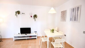 Ein modernes Wohnzimmer mit Flachbildfernseher, weißen Möbeln und Zimmerpflanzen.