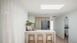 Une cuisine moderne avec un îlot central, des tabourets en bois, un réfrigérateur et une plante en pot.
