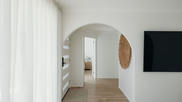 Un couloir doté d’un plancher en bois, de murs blancs et d’une grande œuvre d’art noire sur le côté droit.