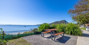 A coastal view with two wooden benches facing the sea, surrounded by greenery and a clear sky. - Bay House Shoal Bay, 36 Government Rd - ducted air conditioning (Shoal Bay)