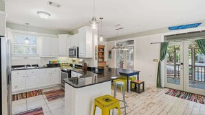 Une cuisine moderne avec des meubles blancs, un plan de travail noir et un îlot central. Le sol est recouvert de tapis rayés aux couleurs vives, et on peut apercevoir un tabouret jaune.