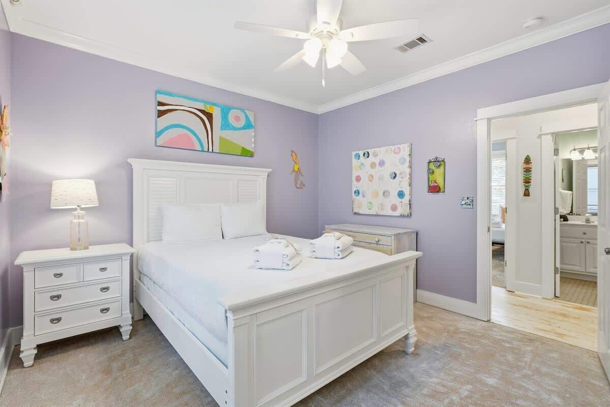 A bedroom with a white bed, nightstands, a ceiling fan, and artwork on the walls.
