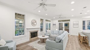 A spacious living room with a fireplace, a grey sofa, a round coffee table, and a ceiling fan. - Sunny Day- Minutes to Beach- Heated Pool- 4 Bikes (Santa Rosa Beach)