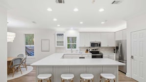 A modern kitchen with white cabinetry, a large island with bar stools, stainless steel appliances, and recessed ceiling lighting. - Sunny Day- Minutes to Beach- Heated Pool- 4 Bikes (Santa Rosa Beach)