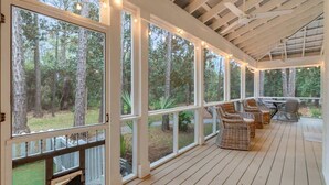 A covered outdoor deck with large windows, wicker furniture, and a view of the surrounding forest. - Sunny Day- Minutes to Beach- Heated Pool- 4 Bikes (Santa Rosa Beach)