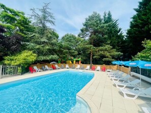 Une piscine entourée d’arbres, avec des chaises longues et des parasols.