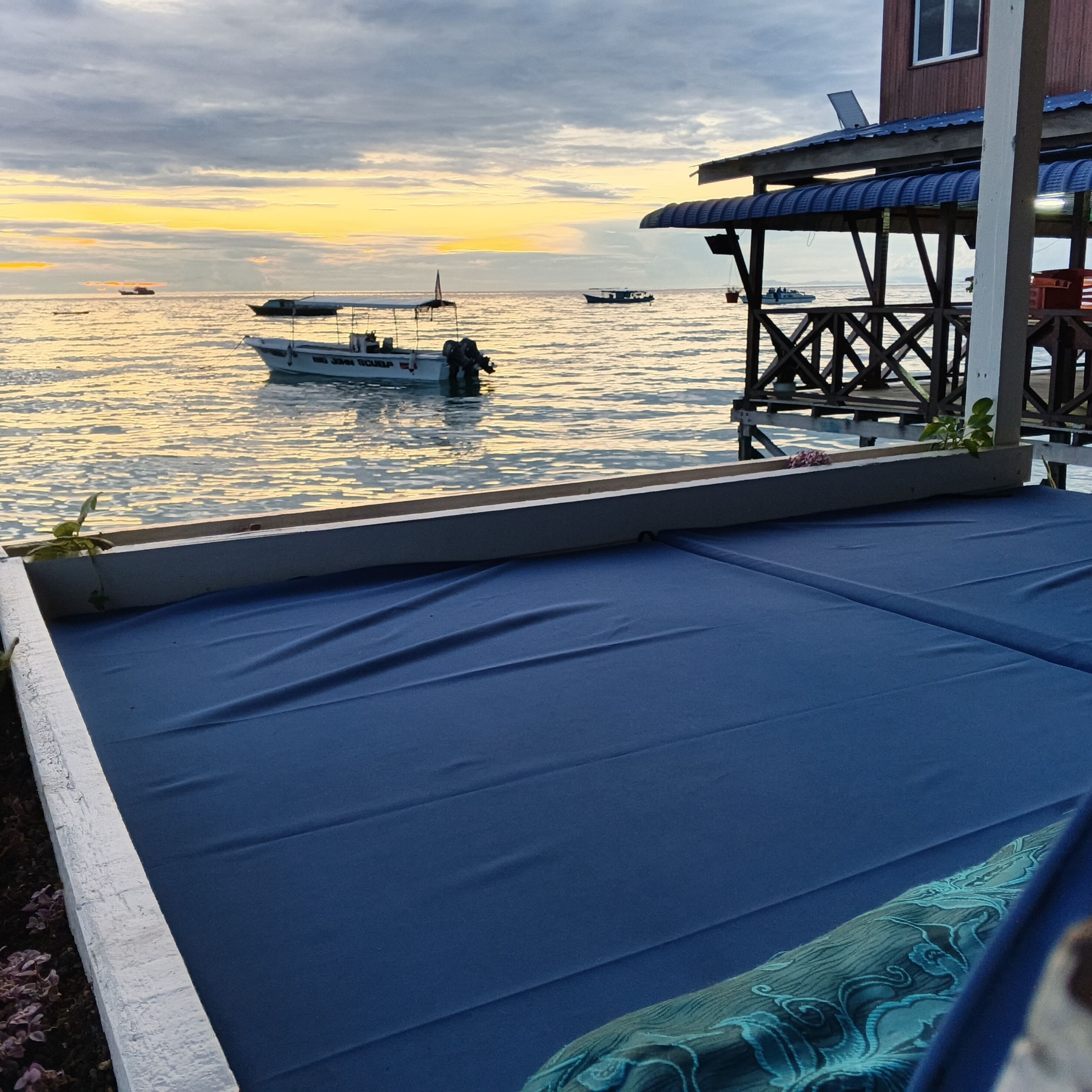 Vista desde un balcón sobre una masa de agua con barcos, una estructura de madera y un área de descanso cubierta.