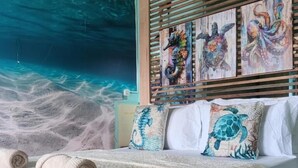 A bedroom with a large mural of the ocean, wooden slats, and multiple pillows with sea turtle designs. - Turtle Garden Lodge  (Mabul Island)