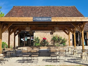 A covered outdoor seating area with a sign reading 'LA PAUSE COQUETTE' and a rustic building with a tiled roof in the background. - Cozy mobile home with terrace, 4 people (La Douze)