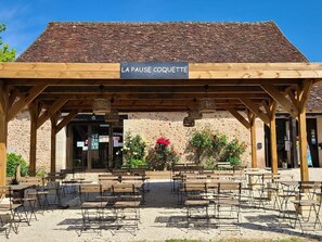 A covered outdoor seating area with a sign reading 'LA PAUSE COQUETTE' and a rustic building with a tiled roof in the background. - Mobile home for 5 with terrace and equipped kitchen (La Douze)