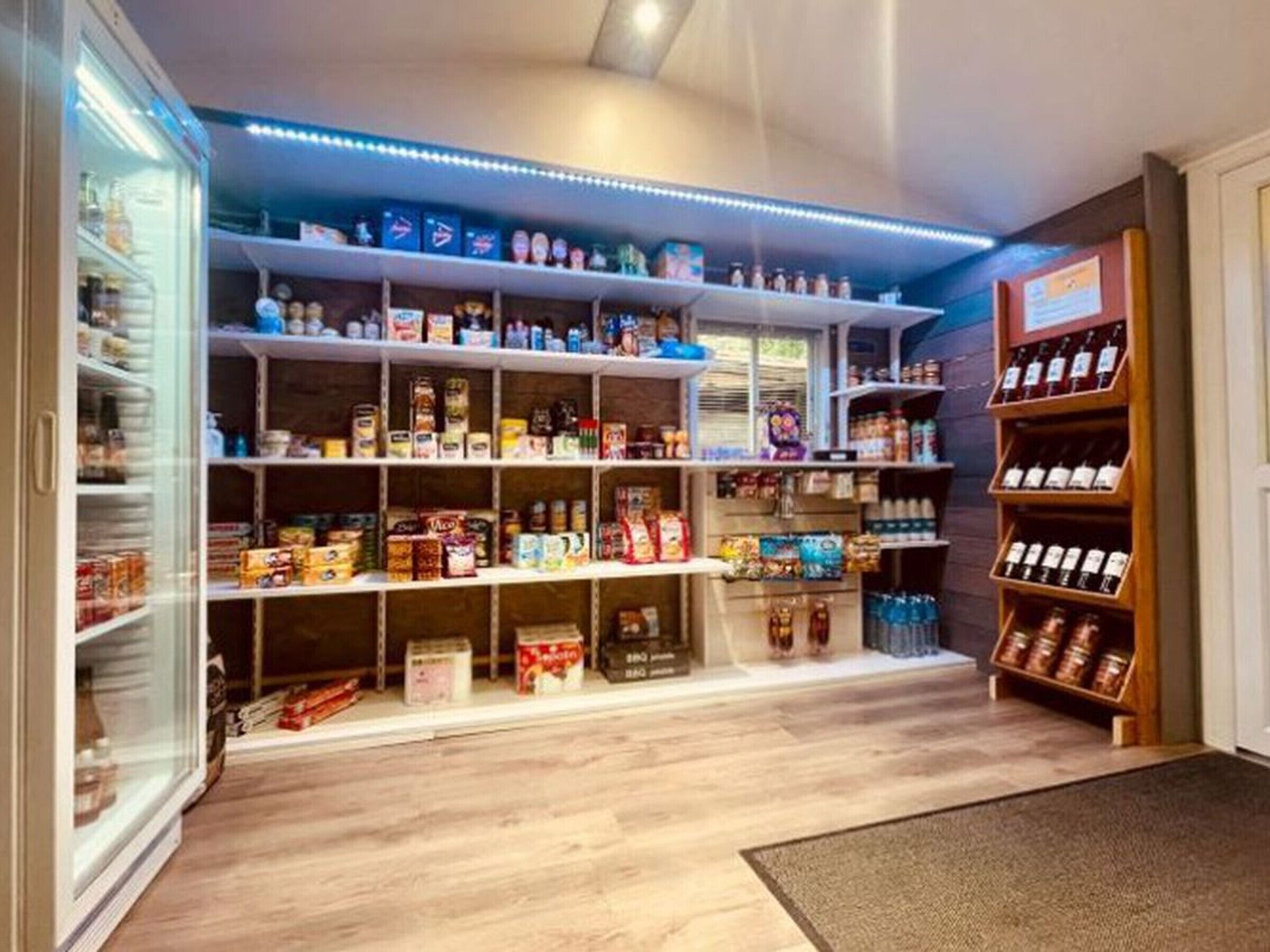 A compact storage area with shelves and a refrigerator, containing various food items and beverages.