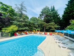 A swimming pool with lounge chairs and umbrellas, surrounded by trees.