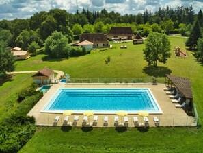 Vista aérea de una piscina con sillas de descanso y sombrillas, rodeada por una cerca y casas en un entorno rural.