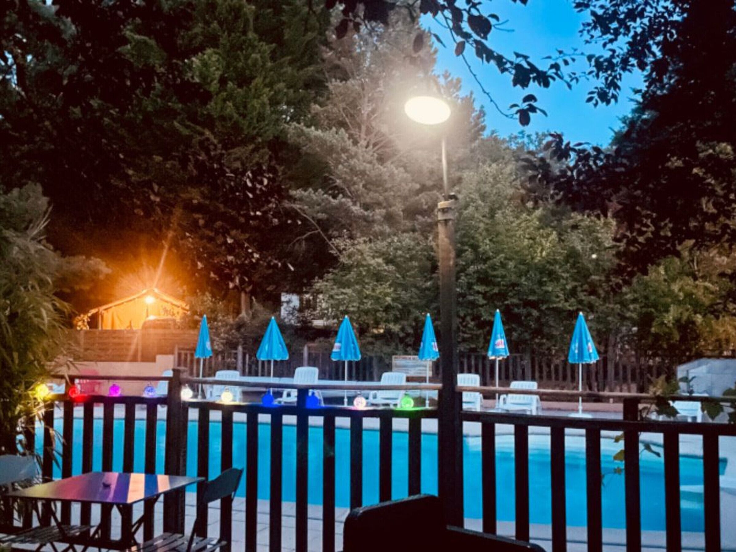A pool area with a fence, umbrellas, and a table with chairs.