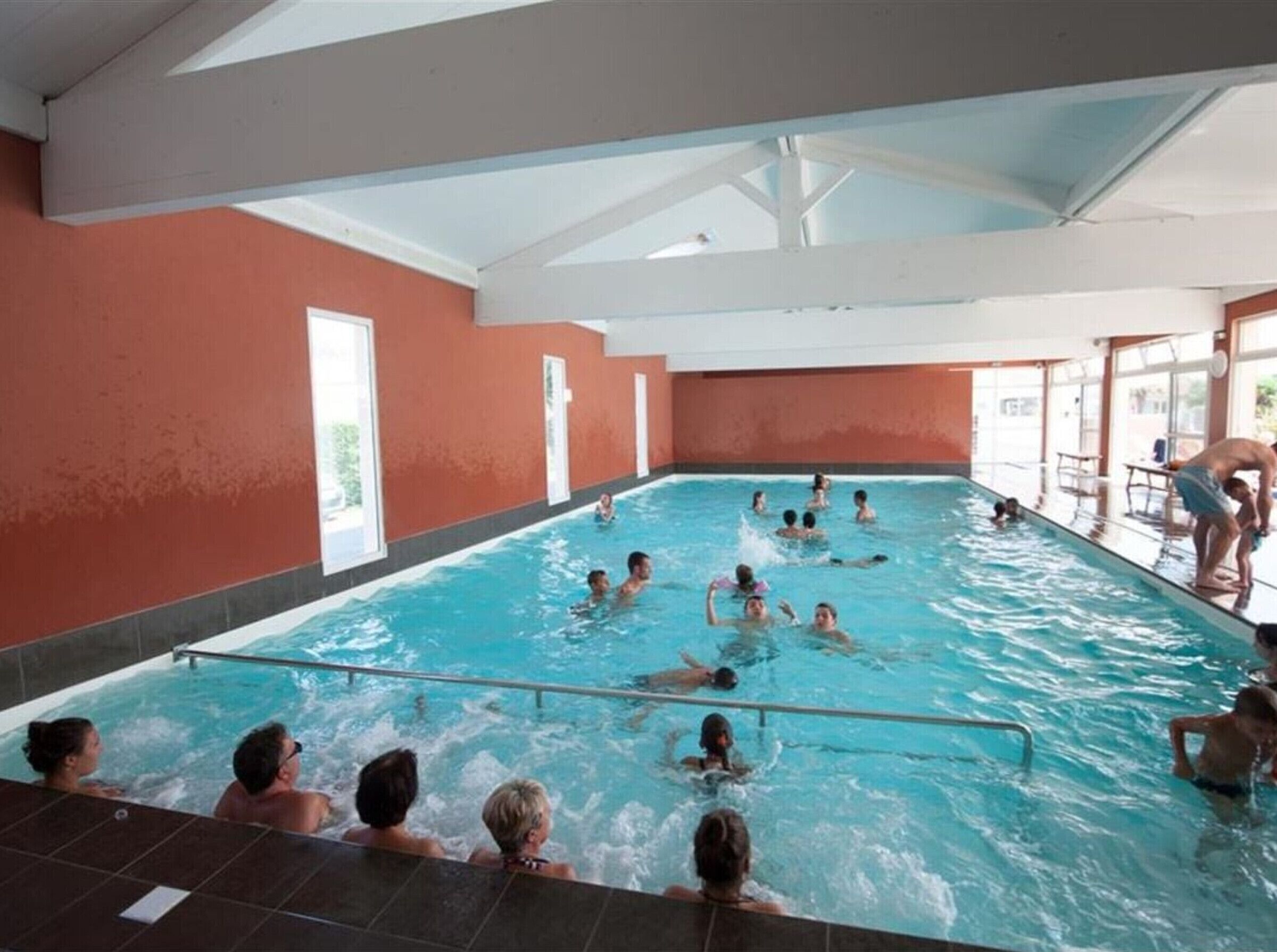 En inomhuspool med flera banor, en livräddarstol och ett område vid poolkanten med ett bord och stolar.