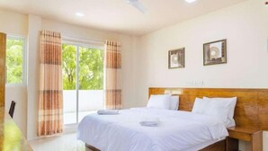 A hotel room with a large bed, a wooden headboard, and a view of greenery outside. - Oceanvine Maldives (Mahibadhoo)