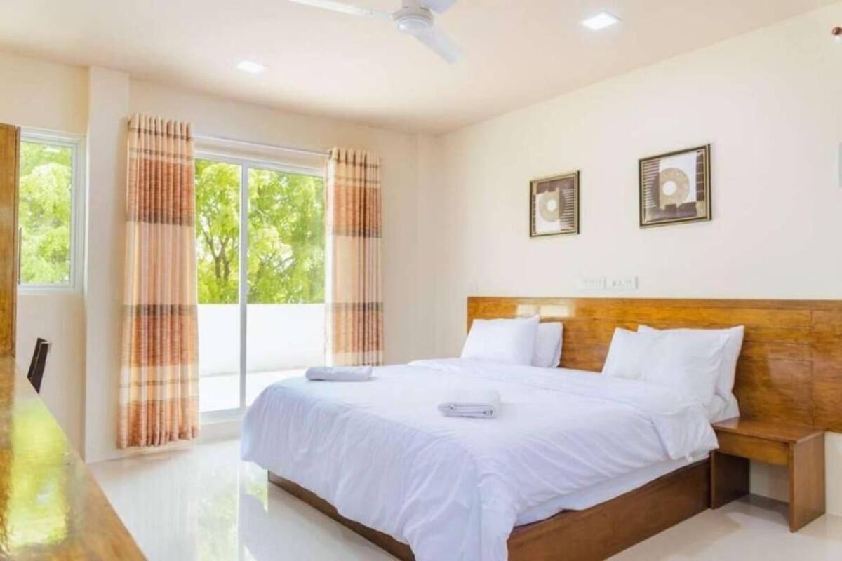 A hotel room with a large bed, a wooden headboard, and a view of greenery outside.