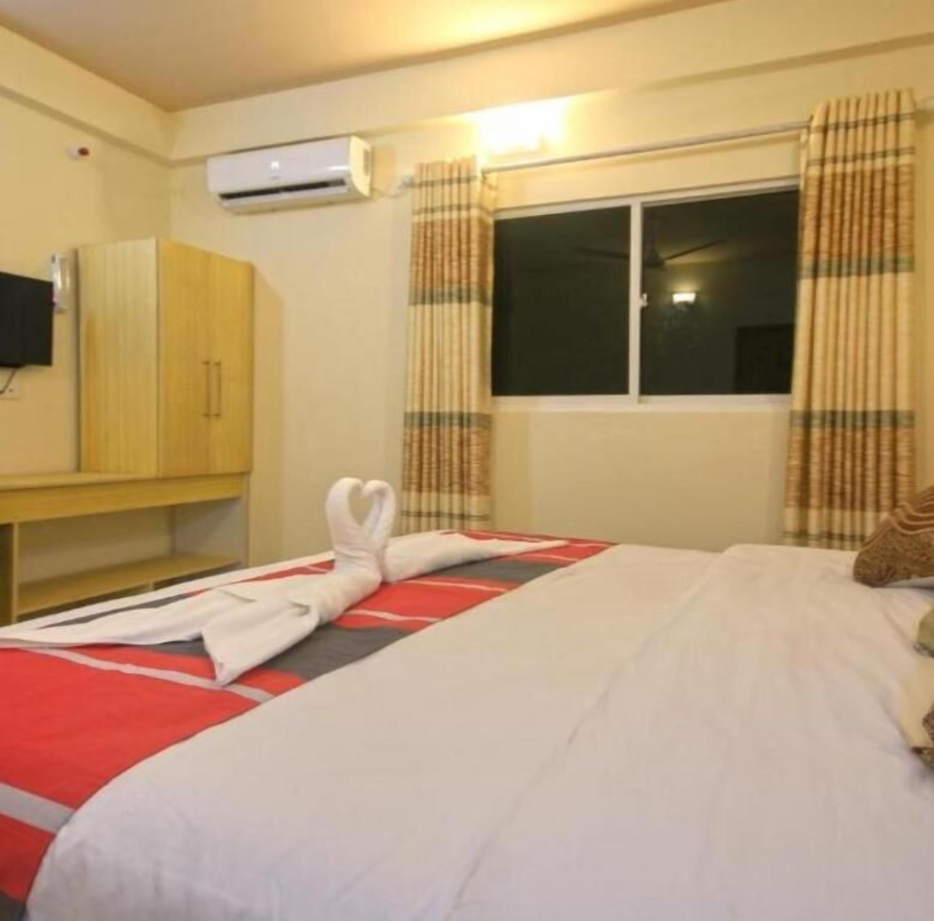 Een hotelkamer met een bed, een kledingkast, een airconditioning en een raam met gordijnen.