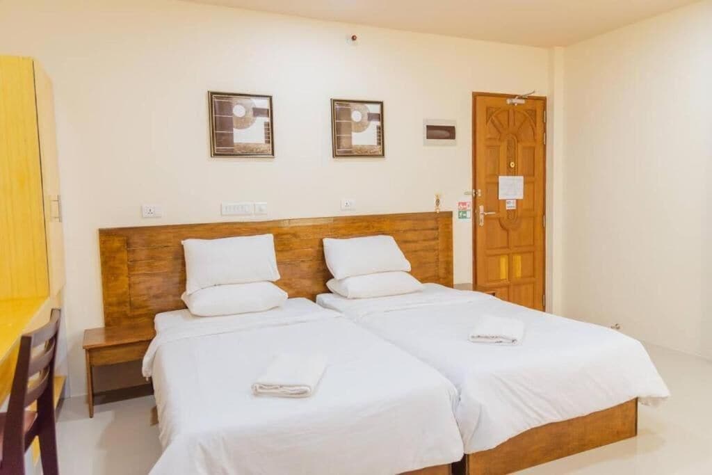 Une chambre d’hôtel avec deux lits simples, une tête de lit en bois, une petite table de chevet et une armoire en bois.
