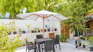 An outdoor patio with a table and chairs, surrounded by potted plants and a white wall. - Oceanvine Maldives (Mahibadhoo)