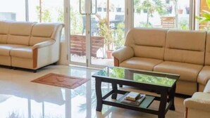 A spacious room with two beige sofas, a glass coffee table, and large windows offering a view of greenery outside. - Oceanvine Maldives (Mahibadhoo)