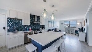 A modern kitchen with white cabinets, a blue backsplash, and a central island with bar stools.