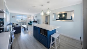 A modern kitchen with a central island, white bar stools, and pendant lighting.
