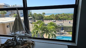 A room with a large window overlooking a pool, palm trees, and a parking lot.