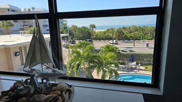 Una habitación con un amplio ventanal que da a una piscina, palmeras y un estacionamiento.