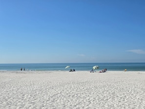 En bred sandstrand med några få personer och strandstolar.
