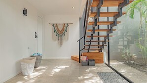 A modern interior with a staircase leading to a balcony, a wall-mounted macrame, and wicker baskets on the floor. - Villa Bernard - luxurious home in Tamarindo, walking distance to the beach& town (Tamarindo)