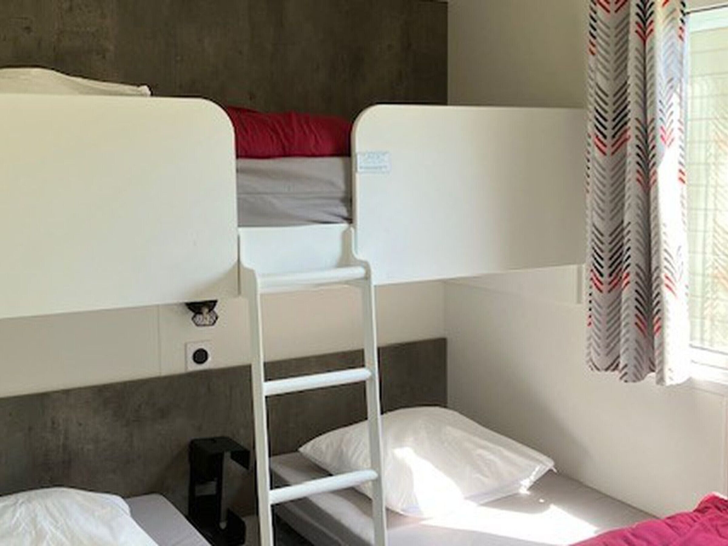 Une chambre avec un lit superposé, une échelle, une fenêtre avec des rideaux et une petite table.