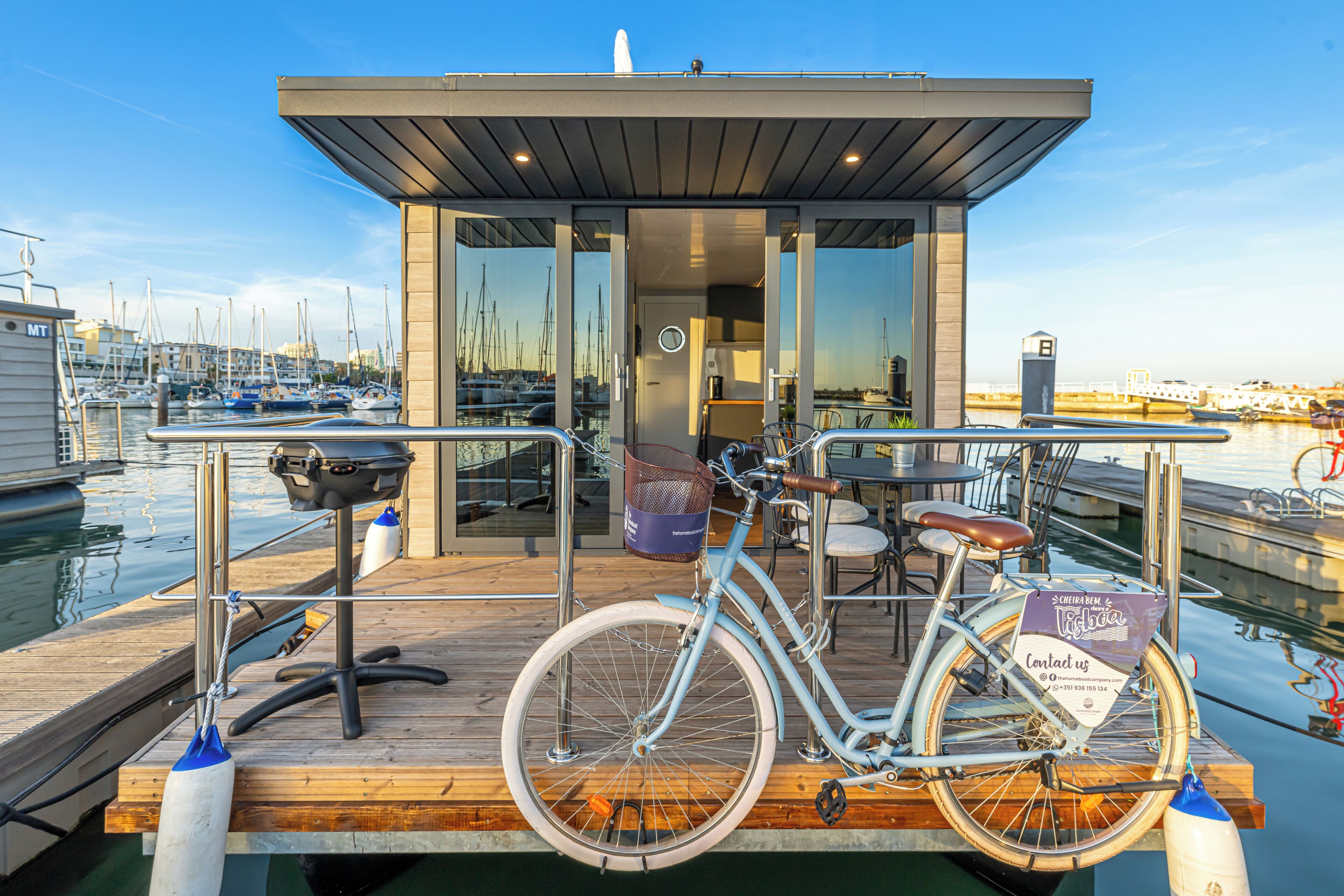A modern boat with a wooden deck, a bicycle, and a small building with glass doors.