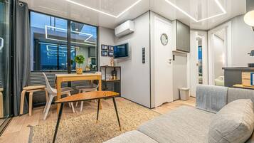 A modern, compact living space with a dining area, a sofa, a TV, and a small kitchen area.