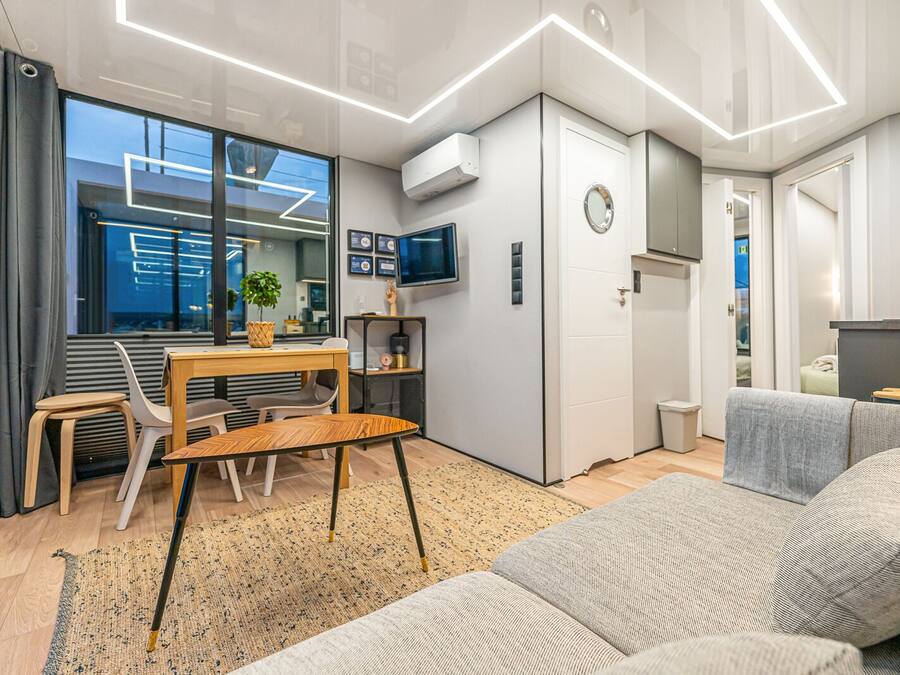 A modern, compact living space with a dining area, a sofa, a TV, and a small kitchen area.