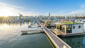 Un puerto deportivo con barcos amarrados, una estructura flotante con terraza y un paisaje urbano al fondo.