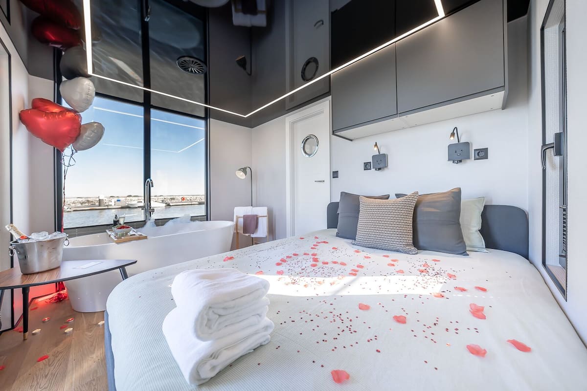 A modern bedroom with a large bed, a view of the sea, and a bucket of champagne.