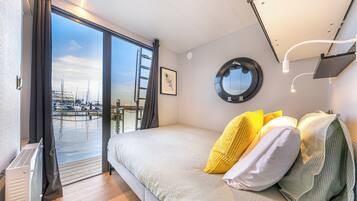 Un dormitorio con cama, ventana, vista a barcos y espejo montado en la pared.