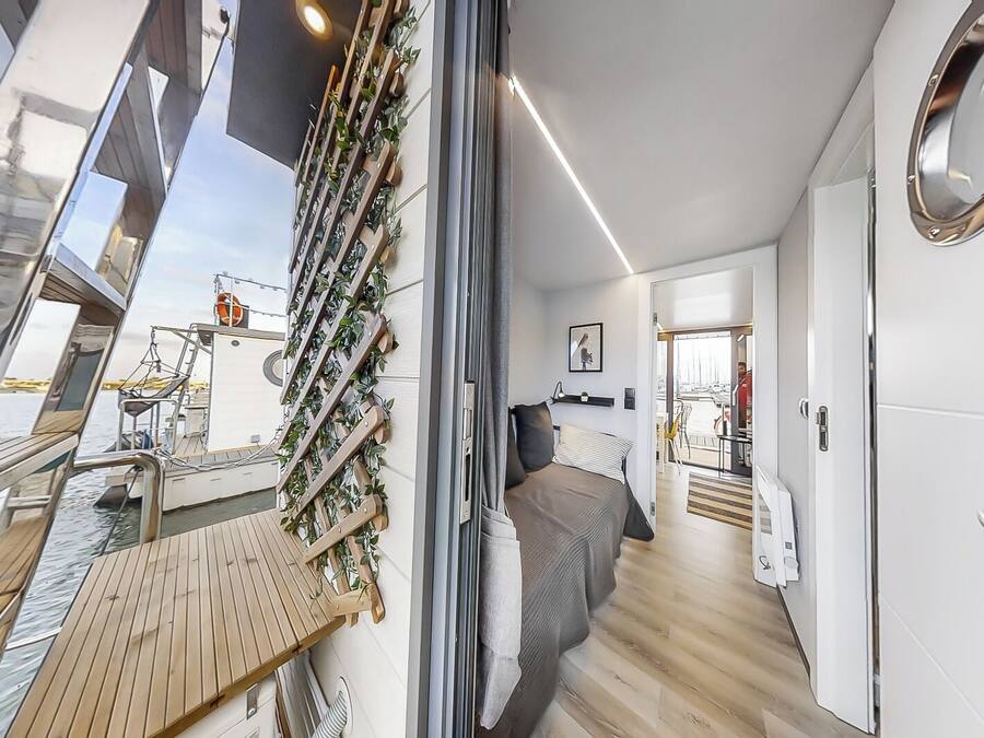 Un interior moderno con una cama, terraza de madera y vista al agua.