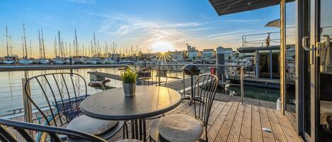 A wooden deck with outdoor seating, overlooking a marina with boats.