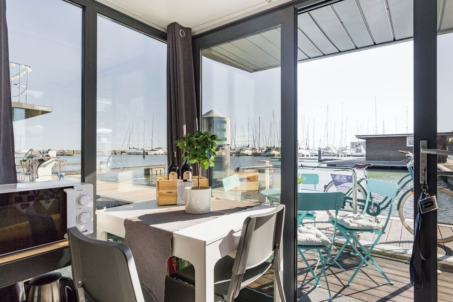 A dining area with a view of a marina, featuring a table with chairs, a potted plant, and a menu stand.