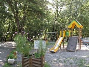 A playground with a slide and climbing structures, surrounded by trees and flowers. - Mobile home with terrace, 3 bedrooms, Neffes (Neffes)
