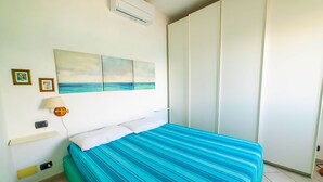 A bedroom with a bed, a wall-mounted air conditioner, a painting of a beach, and a wardrobe. - Apartment Gabbiana Elba Island (Portoferraio)