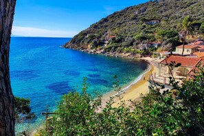 A coastal area with a beach, houses with red-tiled roofs, and a hillside with vegetation. - Apartment Gabbiana Elba Island (Portoferraio)