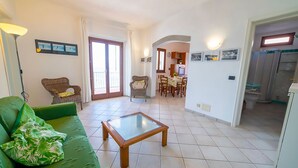 A living room with a green sofa, a glass-top coffee table, and a dining area with wooden chairs and a table. - Apartment Gabbiana Elba Island (Portoferraio)