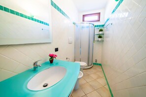 Ein Badezimmer mit einem türkisnen Waschbecken, einer weißen Toilette und einer Duschkabine aus Glas.
