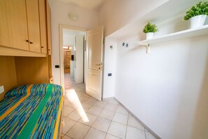 Ein Schlafzimmer mit einem Bett, einem Holzschrank, einer weißen Tür und einer weißen Wand mit einem Regal, auf dem eine Pflanze steht.