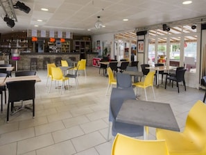 Ein Restaurant mit gelben und grauen Stühlen, einer Bar und Blick ins Freie.