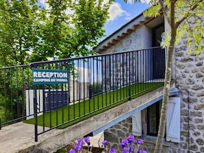 Ein Empfangsschild für einen Campingplatz, ein Steinhaus und eine Treppe mit violetten Blumen.